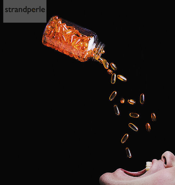 Flasche mit orangefarbenen Medikamentenkapseln  die sich in den Mund eines Mannes entleeren