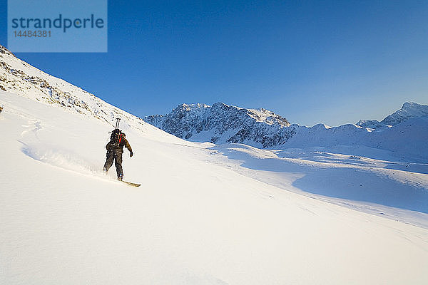 Ein Mann fährt mit dem Snowboard einen Berg in der Nähe von Eagle River hinunter. Winter in Süd-Zentral-Alaska.