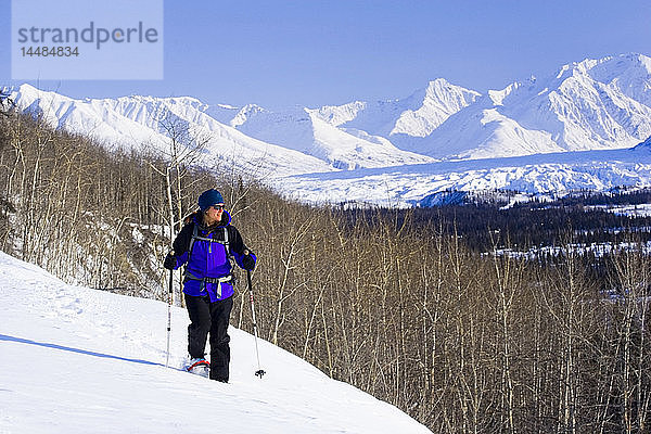 Eine Frau genießt einen sonnigen Tag beim Schneeschuhwandern in den Talkeetna Mountains in der Nähe des Matanuska-Gletschers. Winter in Süd-Zentral-Alaska.