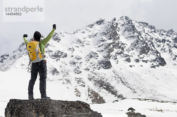 Eine Wanderin steht auf einem großen Felsvorsprung und genießt die Aussicht in den Chugach Mountains in der Nähe des Powerline Pass und des Glen Alps Trailhead  Southcentral  Alaska