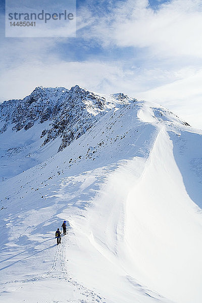 Zwei Schneeschuhläufer erklimmen einen Bergrücken oberhalb des Eagle River im Chugach State Park. Winter in Süd-Zentral-Alaska.