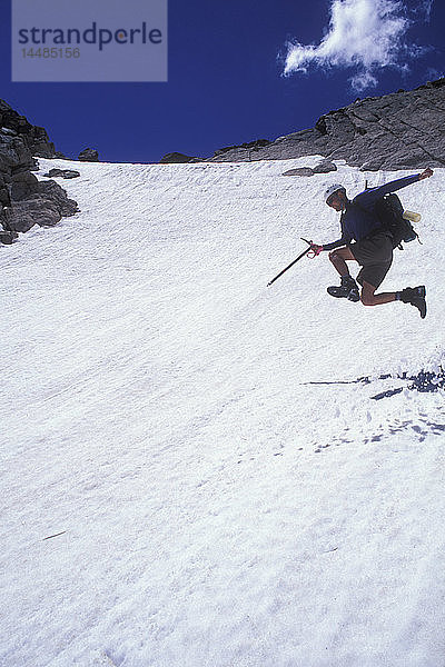 Wanderer mit einem Eispickel  der ein Schneefeld hinunterspringt  Rocky Mountain National Park  Colorado