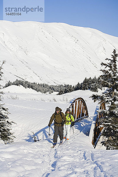 Zwei Skitourengeher fahren über eine Brücke in der Nähe des Turnagain Passes im Chugach National Forest. Winter auf der Kenai-Halbinsel in Alaska.