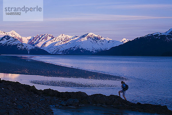 Wanderer in der Abenddämmerung auf einem Bergrücken mit Blick auf den Turnagain Arm und die untergehende Sonne in den Chugach Mountains in Süd-Zentral-Alaska
