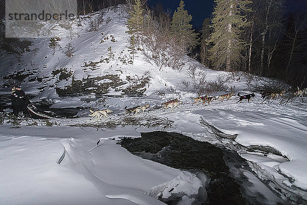 Justin Savidas überquert eine Eisbrücke über den Dalzell Creek in der Nacht während des Iditarod-Schlittenhunderennens 2013  Süd-Zentral-Alaska