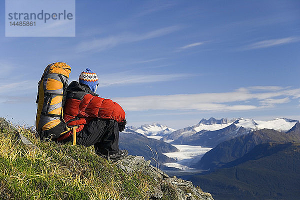 Männlicher Wanderer sitzt auf einem Bergrücken über der Inside Passage und betrachtet Gletscher und Berge im Alaska-Sommer