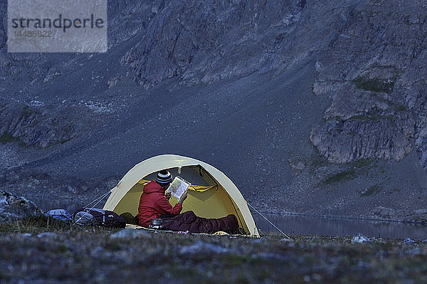 Frau in einem Zelt konsultiert ein GPS und eine Karte beim Zelten am Rabbit Lake  Chugach State Park  Southcentral Alaska  Herbst