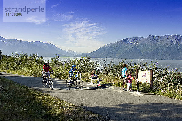 Eine Familie liest ein Informationsschild am Coastal Trail in der Nähe von Indian  AK  während Radfahrer vorbeifahren. SC Alaska Sommer.