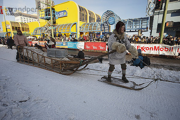 Ein Mann fährt auf dem Gee Pole   während Musher Dean Osmar den Schlitten fährt  um einen Wells Fargo Frachtschlitten während des Iditarod 2014 Ceremonial Starts in der Innenstadt von Anchorage  Alaska  nachzustellen und zu demonstrieren.