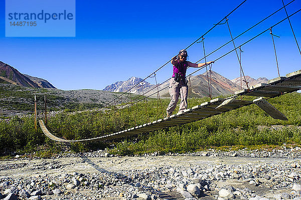 Eine Frau geht auf einer Hängebrücke über den College Creek zum Gulkana-Gletscher  Southcentral Alaska  Sommer/n