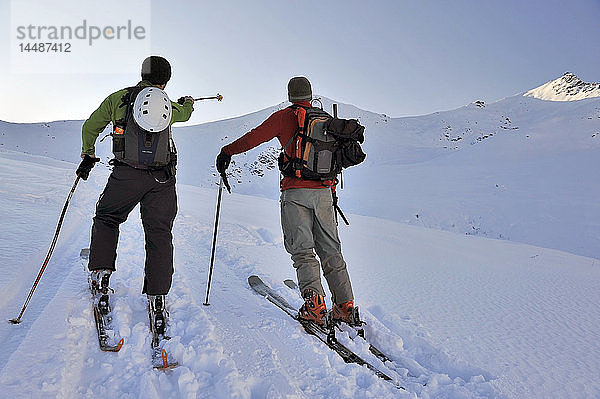 Ein Skitourengeher zeigt einem anderen Skifahrer einen Gipfel  während er eine Pause am Hatcher Pass  Southcentral  Alaska  einlegt