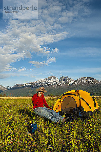 Ein Mann spricht auf seinem Campingplatz im Palmer Haystack Flats Wildlife Refuge in der Nähe von Rabbit Slough in Süd-Zentral-Alaska mit einem Mobiltelefon