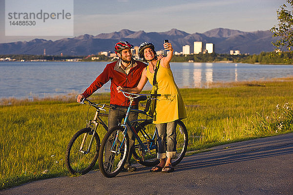 Radfahrer  die sich ausruhen und Selbstporträts entlang des Tony Knowles Coastal Trail mit der Skyline von Anchorage im Hintergrund machen  Southcentral Alaska