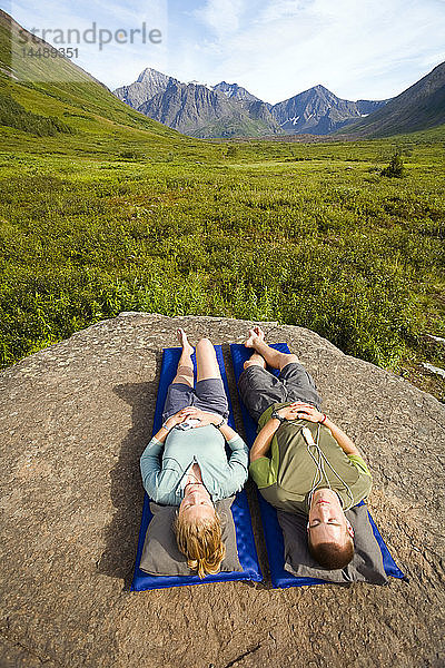 Männlicher und weiblicher Wanderer entspannen sich auf einer Isomatte und hören Musik auf dem iPod entlang des South Fork Eagle River Trail Chugach State Park Alaska Sommer