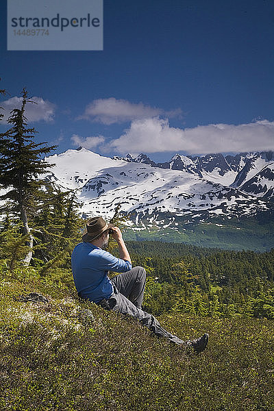 Mann ruht sich auf der Tundra aus und genießt die Aussicht auf die Kenai-Berge entlang des Lost Lake Trail in der Nähe von Seward  Alaska  im Sommer