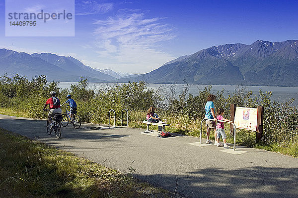 Eine Familie liest ein Informationsschild am Coastal Trail in der Nähe von Indian  AK  während Radfahrer vorbeifahren. SC Alaska Sommer.