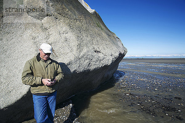 Mann mit Mobiltelefon neben einer großen Felsformation  Clam Gulch  Kenai-Halbinsel  Southcentral Alaska