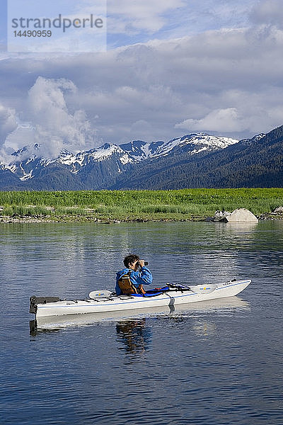 Frau betrachtet die Landschaft durch ein Fernglas vom Seekajak aus Holkham Bay Tracy Arm Südost Alaska Sommer