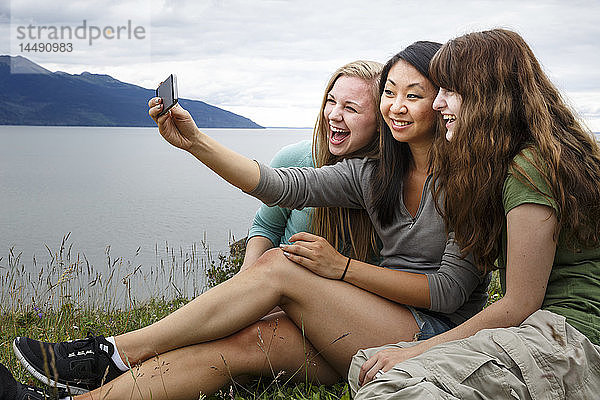 Drei multikulturelle junge Frauen machen ein Gruppen-Selfie während einer Wanderung entlang des Turnagain Arm  Southcentral Alaska  Sommer