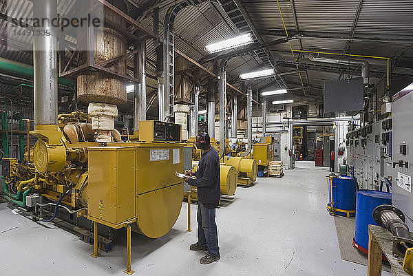 Ein männlicher hispanischer Arbeiter inspiziert einen gelben Dieselgenerator in einem Elektrizitätswerk  Prudhoe Bay  arktisches Alaska  USA  Sommer