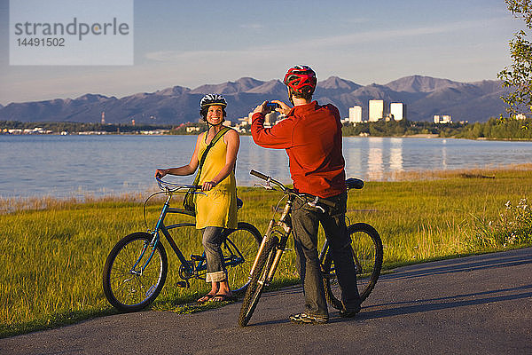 Radfahrer  die sich ausruhen und Selbstporträts entlang des Tony Knowles Coastal Trail mit der Skyline von Anchorage im Hintergrund machen  Southcentral Alaska