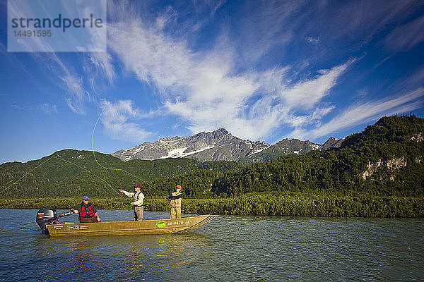 Mann und Frau beim Fliegenfischen auf Lachs vom Boot aus auf dem Big River Lakes mit Angelführer und den Chigmit Mountains im Hintergrund im Sommer in Süd-Zentral-Alaska