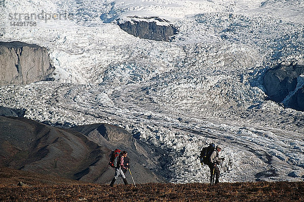 Zwei Rucksacktouristen wandern über ein Plateau mit dem Mount Wrangell im Hintergrund im Wrangell-St.Elias National Park in Süd-Zentral-Alaska. Herbst