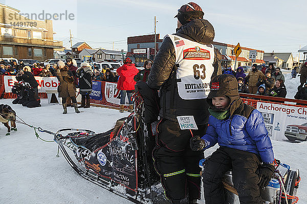 Aaron Burmeister´s Sohn fährt auf dem Schlittenwagen  während Aaron sein Team zum Hundeplatz führt  nachdem er beim Iditarod 2015 den dritten Platz belegt hat