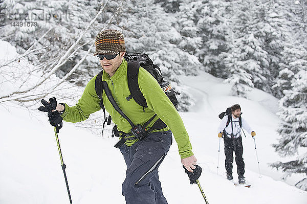 Ein Skifahrer und ein Snowboarder fahren einen Abhang am Turnagain Pass in Southcentral Alaska hinauf