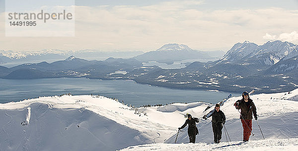 Skifahrer wandern auf dem Westgrat des Eaglecrest-Skigebiets  um zu den Pisten außerhalb des Skigebiets zu gelangen  mit Stephens Passage und Admiralty Island im Hintergrund  Südosten  Alaska