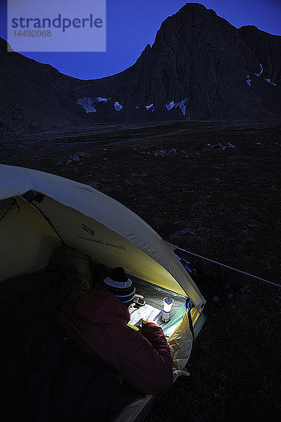 Frau in einem Zelt in der Abenddämmerung konsultiert ein GPS und eine Karte beim Zelten am Rabbit Lake  Chugach State Park  Southcentral Alaska  Herbst