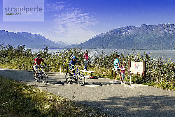 Eine Familie liest ein Informationsschild am Coastal Trail in der Nähe von Indian  AK  während Radfahrer vorbeifahren. SC Alaska Sommer.