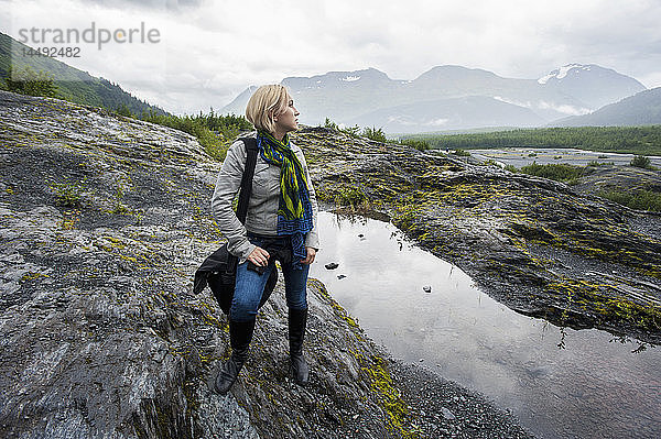 Frau steht auf einer Felsenlandschaft in der Nähe von Seward mit den Kenai Mountains im Hintergrund  Kenai-Halbinsel  Süd-Zentral-Alaska