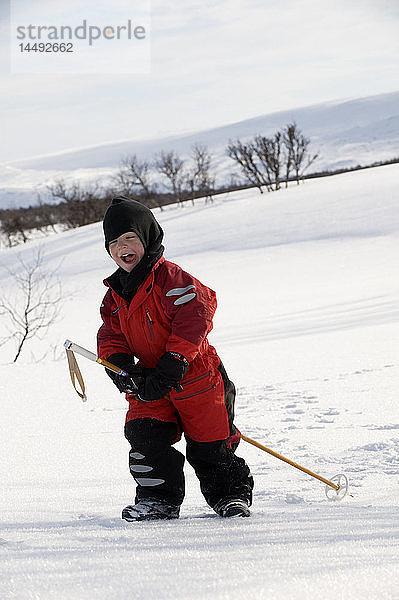 Junge spielt mit Wanderstock im Schnee