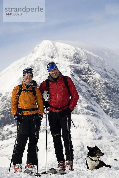 Zwei Menschen mit Hund in der Nähe eines schneebedeckten Berges