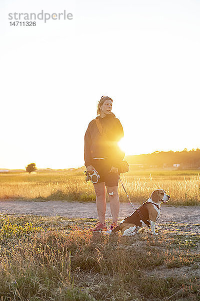 Frau führt Hund bei Sonnenuntergang aus