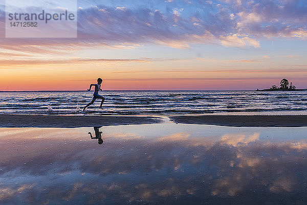 Junge läuft am Strand bei Sonnenuntergang