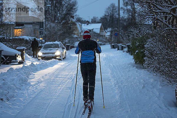 Mann beim Skilanglauf im Dorf in der Abenddämmerung