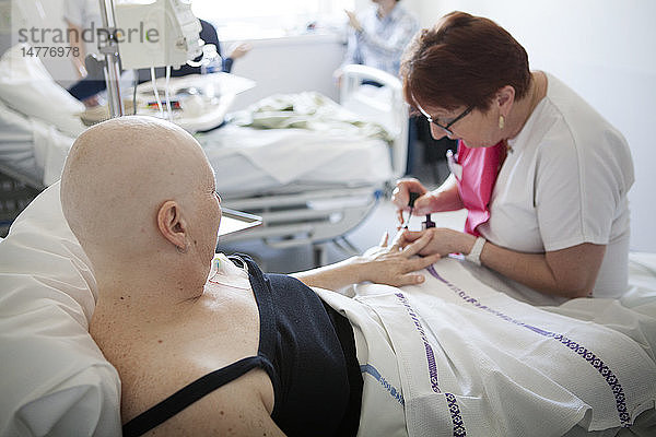 Reportage in der onkologischen Abteilung einer Tagesklinik in Frankreich. Die Hilfskrankenschwester Marie-Cecile arbeitet hier drei Tage in der Woche als Krankenhauskosmetikerin. Sie bietet krebskranken Frauen Schönheitsbehandlungen und Lösungen zur Bewältigung der Nebenwirkungen von Krebsbehandlungen an. Diese Momente eignen sich gut für persönliche Gespräche. Sie gibt einer Patientin eine Schönheitsbehandlung während einer Chemotherapie.
