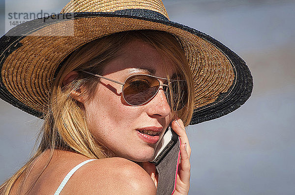 Junge Frau telefoniert am Strand.