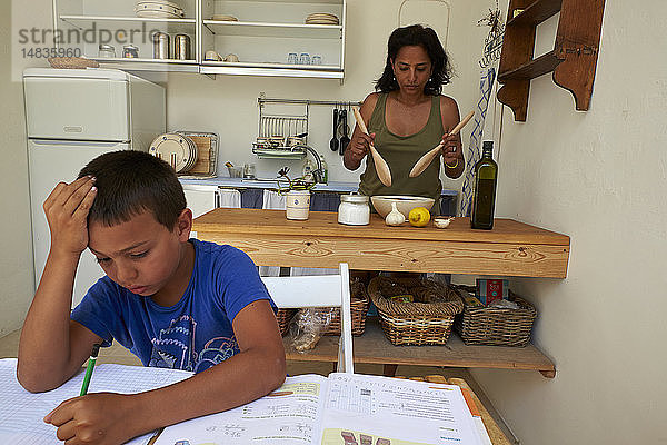 Junge macht Hausaufgaben  während seine Mutter kocht.