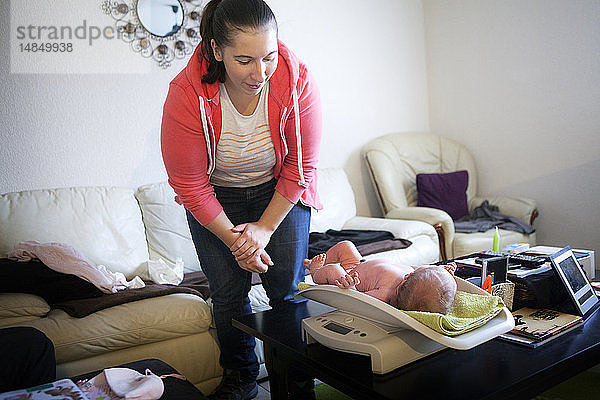 Reportage über eine unabhängige Hebamme bei Hausbesuchen nach der Geburt. Die Hebamme wiegt das neugeborene Baby.