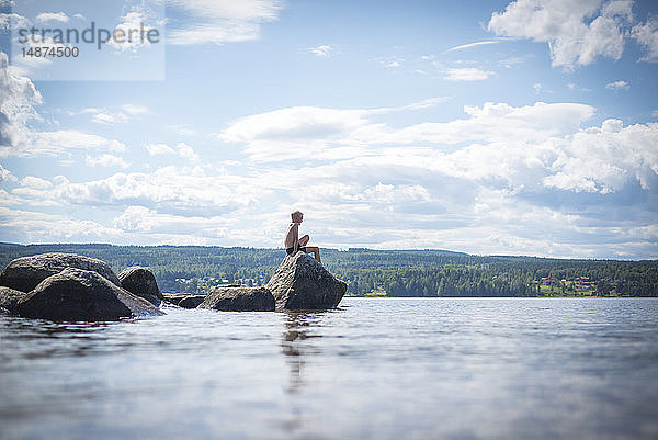 Junge sitzt auf einem Felsen am Meer
