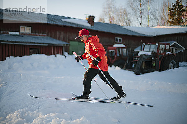 Junge beim Skifahren vor einer Scheune