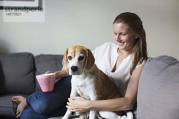 Frau sitzt mit Hund auf dem Sofa