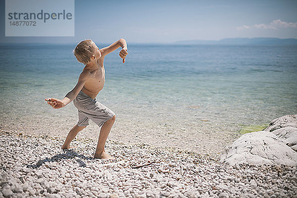 Junge wirft Steine am Strand