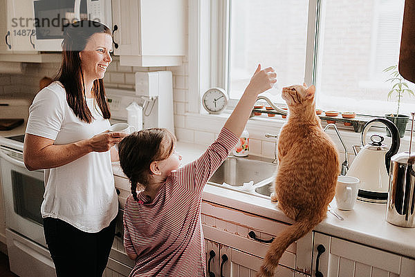 Mutter beobachtet Tochter beim Spielen mit Katze auf Küchenarbeitsplatte