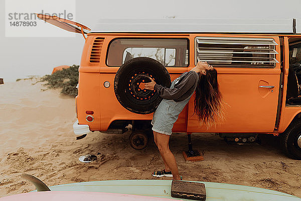 Junge Frau hält Reifen eines Wohnmobils am Strand hoch  Jalama  Kalifornien  USA