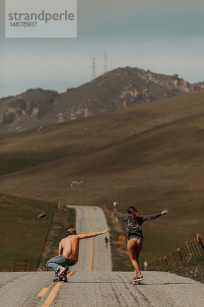 Junges Skateboardfahrerpaar beim Skateboarden auf der Landstrasse  Rückansicht  Jalama  Kalifornien  USA