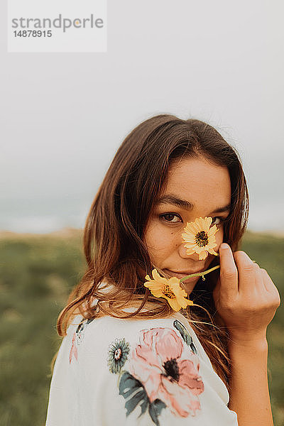 Junge Frau hält an der Küste Wildblumen vor dem Gesicht  Porträt  Jalama  Kalifornien  USA